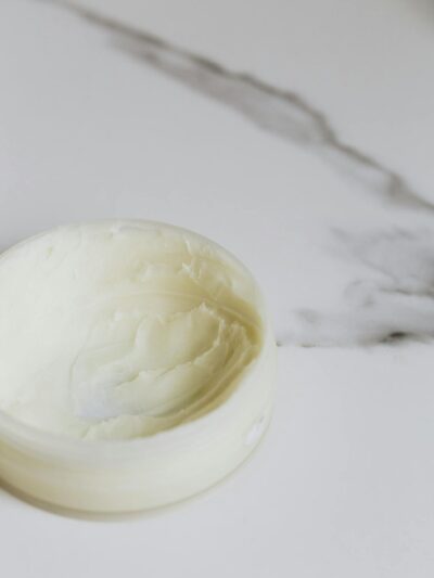 Close-up of a skincare cream in a round container on a marble surface.